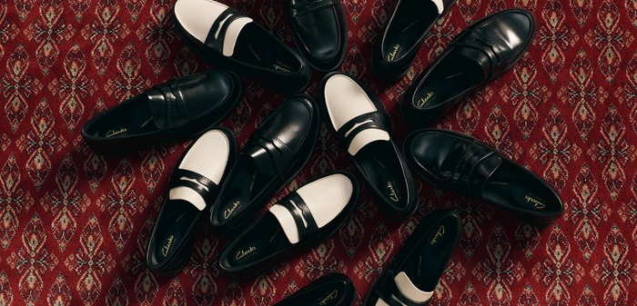 Plusieurs paires de mocassins en cuir noir et blanc disposées sur un tapis rouge à motifs.