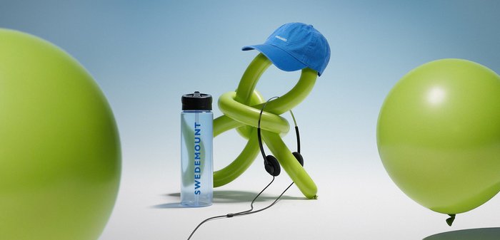 Dve zviti zeleni baloni, eden nosi modro kapo in črne slušalke, poleg prozorne plastenke z vodo z etiketo »Swedemount«, v bližini pa sta še dva zelena balona.