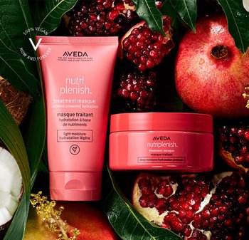 Aveda Nutriplenish-behandlingsmask i en rosa tub och burk, placerad mot granatäpple och gröna blad, vilket visar en livfull, naturlig estetik.