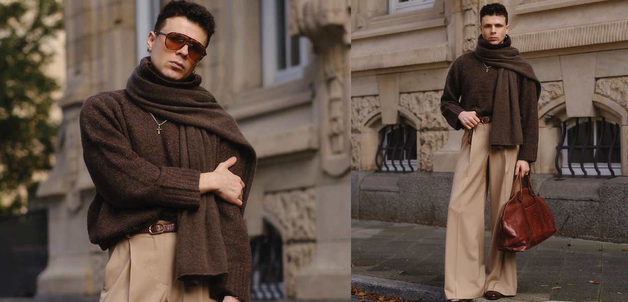 Ruskea neulottu villapaita, jossa on leveät hihat, laskostettu ruskea huivi, vaaleanbeige leveälahkeiset housut ja ruskea nahkalaukku. Aurinkolasit ja ristiriipus.