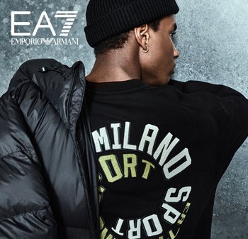 Veste rembourrée noire à col haut, portée par-dessus un sweat-shirt noir arborrant un grand lettrage "MILANO SPORT" en blanc et vert.