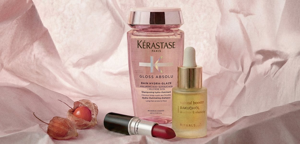 Kérastase Gloss Absolu -shampoo, Rituals Bakuchiol -ihonhoitovahvistinpullo ja MACin punainen huulipuna aseteltuina rypytetyn vaaleanpunaisen kankaan päälle, kuivattujen kuorittujen tomaattien kanssa.