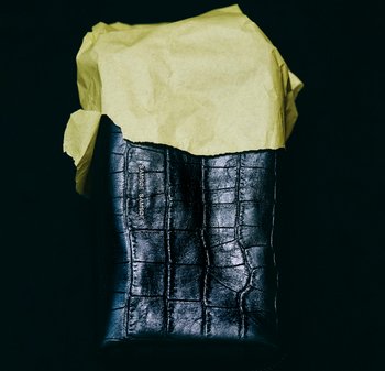 Schwarze Lederetui mit Krokodilprägung, teilweise mit gelbem Seidenpapier bedeckt. Mit Logo an der Seite versehen.