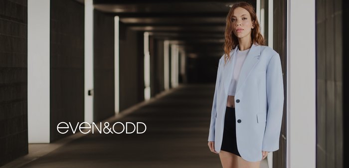 Lichtblauwe oversized blazer met twee zwarte knopen, gecombineerd met een witte crop top en zwarte minirok, geplaatst in een moderne gang.
