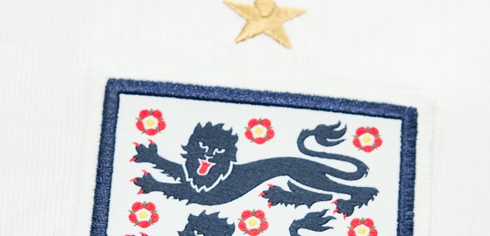 Blason de football de l’Angleterre avec trois lions, des roses rouges et une étoile dorée au-dessus sur tissu blanc.
