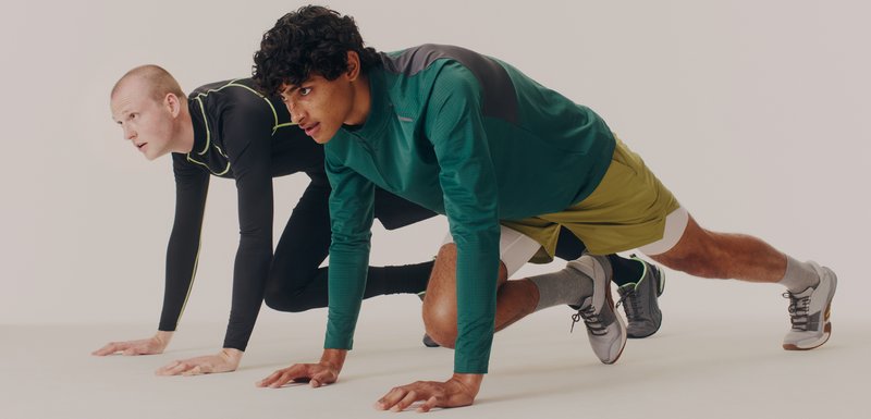 Deux athlètes masculins en position de départ. L'un porte un haut à manches longues noir avec des accents verts ; l'autre porte un haut vert et un short jaune.