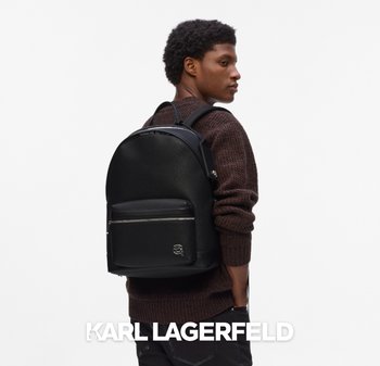 Mochila de cuero negra con acabado texturizado, forma redondeada, bolsillo con cremallera en la parte frontal y logo sutil; llevada por una persona con un suéter de punto marrón.