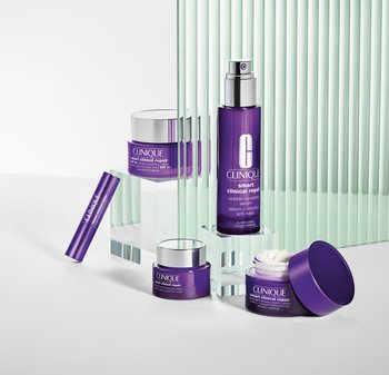 Fioletowe kosmetyki do pielęgnacji na odbijającej się powierzchni, z błyszczącymi słoikami i butelką z pompk ą z metalicznymi akcentami oraz gładką teksturą.