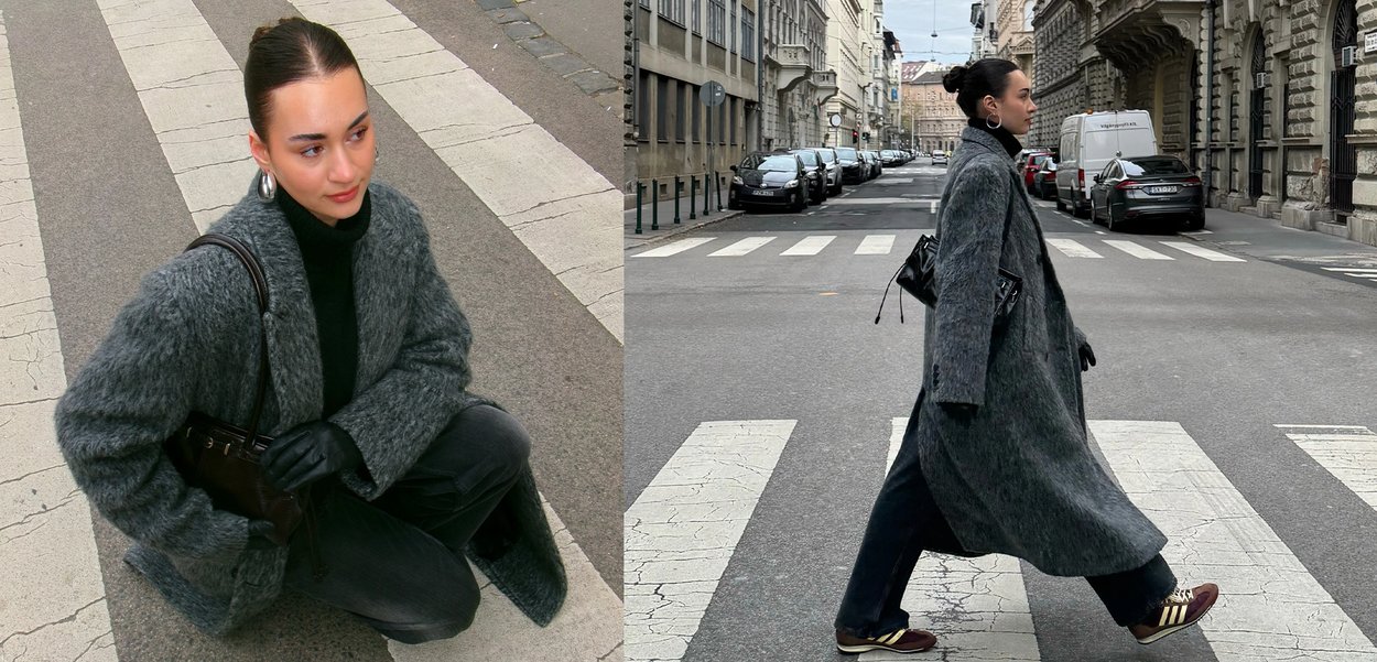 Γυναίκα με χτενισμένα προς τα πίσω μαλλιά φορά γκρι χνουδωτό παλτό, μαύρο πουλόβερ ζιβάγκο, γάντια και αθλητικά παπούτσια ενώ κάθεται και διασχίζει έναν δρόμο στην πόλη.