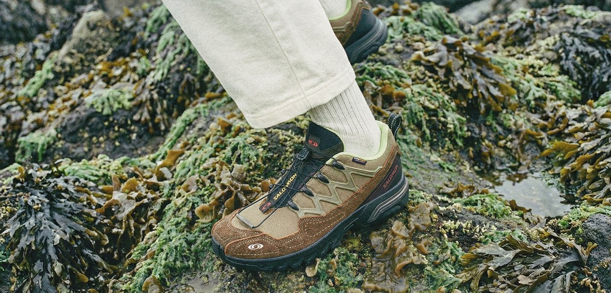 Brūna un zaļa pārgājienu apavu ar teksturētu zamšādas un sieta augšdaļu, izstrādāta atbalstam, ar auklu aizdari un gumijas zoli.