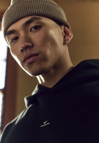 Must musta dressipluus peene logoga rinnal, kombineeritud helepruuni kootud talvemütsiga, esile tuues sileda naha ja neutraalse tausta.