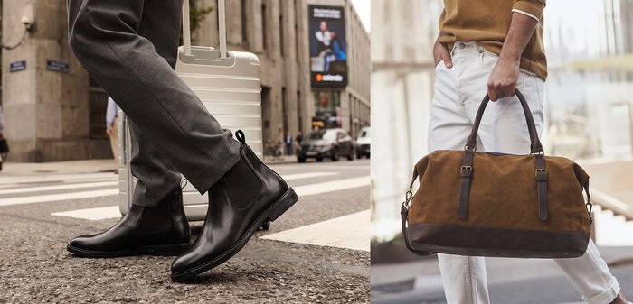 Person wearing black leather ankle boots and gray trousers, pulling a white hard-shell suitcase while walking on a city street crosswalk.