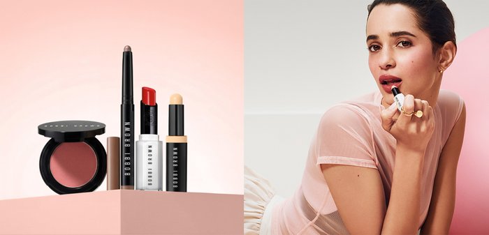 Ulike Bobbi Brown sminkeprodukter vist frem, sammen med en kvinne som påfører rød leppestift mens hun har på seg en gjennomsiktig rosa topp og gullringer.
