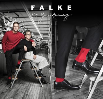 Rote Socken mit Logodetail bilden einen Kontrast zu schwarzen Schuhen und Kleidung. Eine moderne Fabrikumgebung mit industriellen Maschinen im Hintergrund.