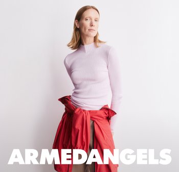 Donna con capelli di media lunghezza che indossa una maglietta a costine color viola chiaro e una giacca rossa legata in vita su uno sfondo bianco.