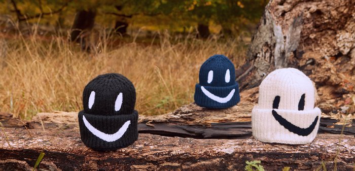 Tre strikkede hue i sort, marineblå og hvid, med store smilende ansigt designs i kontrasterende farver og ribbet tekstur.