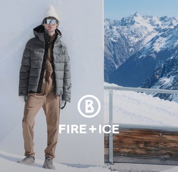 Kurtka puchowa w ciemnoszarym kolorze, nałożona na jasnobeżową bluzę termalną i pasujące spodnie. Szare sneakersy dopełniają strój w górzystym, ośnieżonym tle.