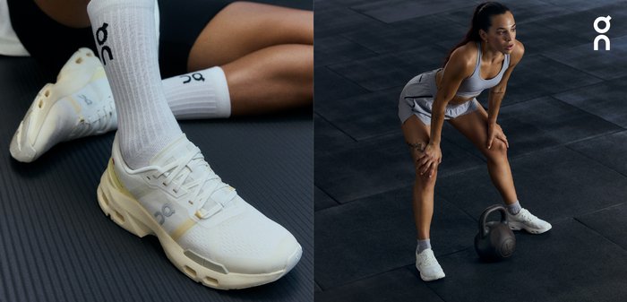 Vita sportskor av vita färg med ett meshinmaterial, gula accenter och detaljerad sula för grepp. Grå gummikettlebell på ett mörkt strukturerat golv.