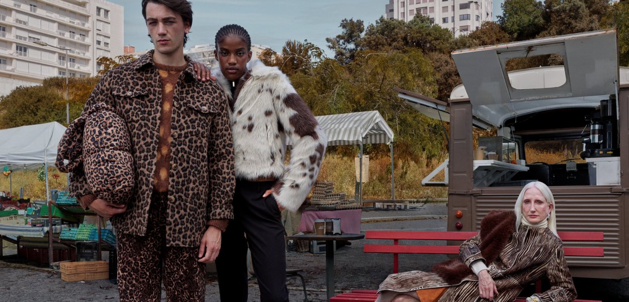 Leopard print fur jacket and pants on one model; spotted fur jacket on another; textured brown striped coat on seated model; urban backdrop.