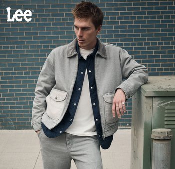 Grå jeansjacka med två framfickor, kombinerad med en marinblå skjorta och en vit T-shirt. Enkel design och avslappnad passform mot en tegelvägg som bakgrund.