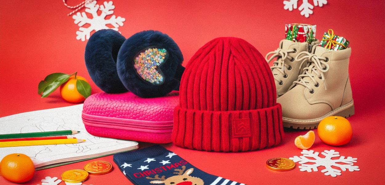 Rote gerippte Strickmütze, marineblaue Kunstfell-Ohrenschützer mit glitzernden Herzen, beige Ankle Boots, rosa strukturiertes Täschchen, grüne und gelbe Bleistifte, orangefarbene Früchte.