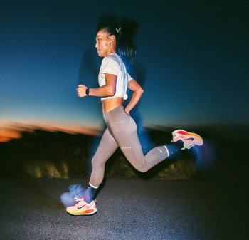 Sportbekleidung: eng anliegende graue Leggings und ein weißes T-Shirt mit kurzen Ärmeln. Helle, mehrfarbige Laufschuhe. Bewegungsunschärfe durch das Laufen.