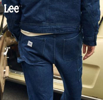 Dark blue denim jacket and trousers, featuring large pockets and a Lee logo patch. The fabric has a textured finish with stitched detailing.