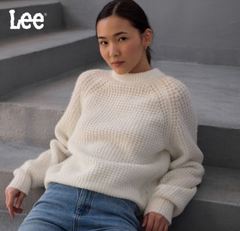 Kvinna i en vit strukturerad tröja och blå jeans, sittande på grå betongtrappor, med "Lee"-logotypen i det övre vänstra hörnet.