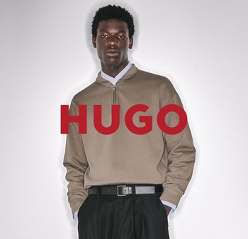 Pull-over zippé beige en quart, fabriqué dans un tissu à texture lisse, porté sur une chemise à col. Ceinture noire avec une boucle en argent. Inscription rouge "HUGO".