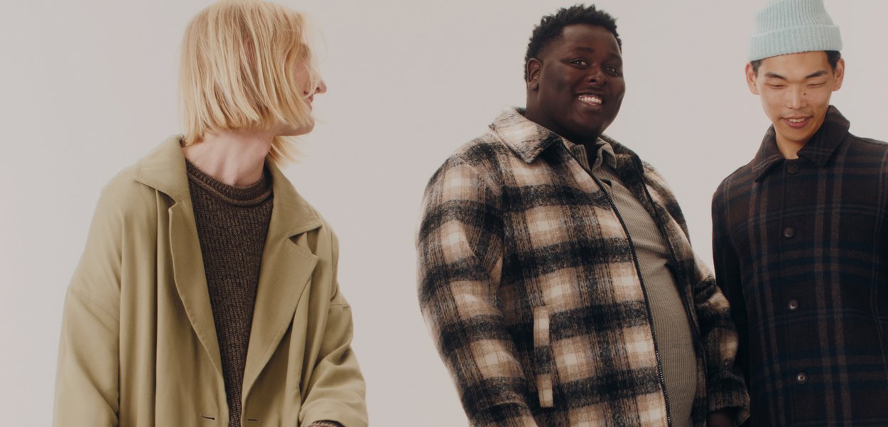 Trei modele poartă îmbrăcăminte exterioară: un palton kaki, o jachetă din lână tartan în bej și negru, și un palton cu model în carouri bleumarin, cu nasturi.