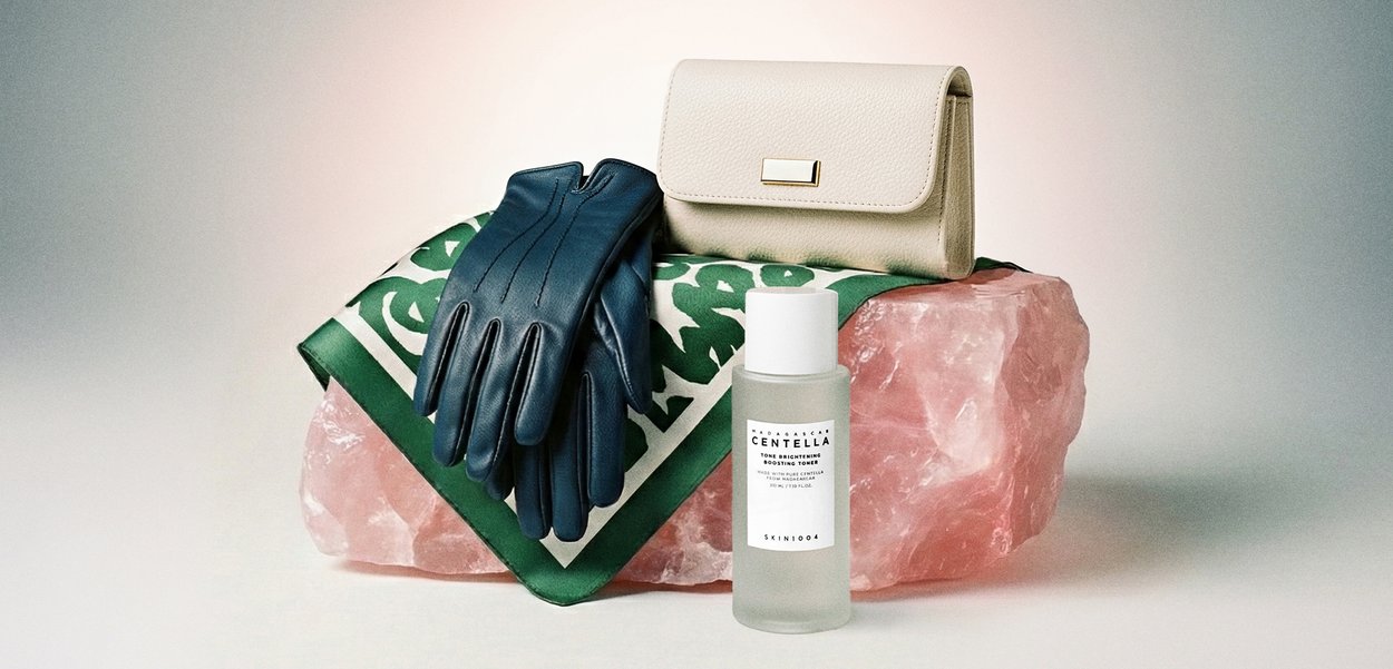 Blå lærhansker, kremfarget lær lommebok, grønt mønstret skjerf på stor rosa krystall, med en flaske Skin1004 Centella toner.