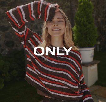 Jonge vrouw die buiten glimlacht, gekleed in een bruin, rood, wit en roze gestreepte trui, met één arm boven haar hoofd geheven.