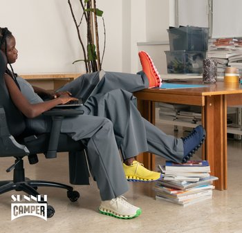 Bunte Schuhe ausgestellt: rote, gelbe, marineblaue und cremefarbene Sneakers mit strukturierten Sohlen, vor einem minimalistischen Arbeitsplatz mit Grünpflanzen.