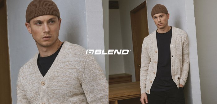 Beige gestrickte Strickjacke mit V-Ausschnitt, Holzknöpfen und gerippten Bündchen, kombiniert mit einem schwarzen Hemd. Getragen mit einer braunen gestrickten Mütze.