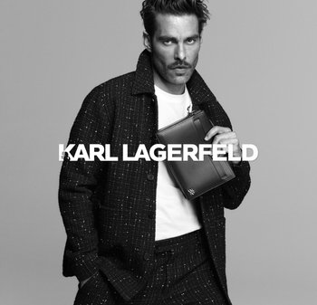 Blazer de tweed negro con textura visible, combinado con una camiseta blanca. El modelo sostiene un elegante estuche para documentos negro con un diseño minimalista.