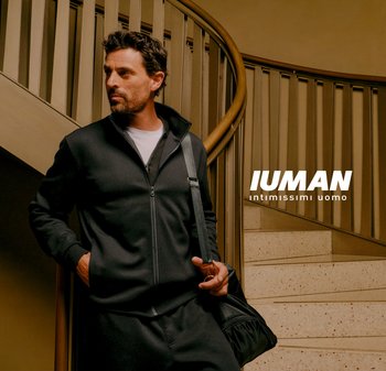 Giacca nera con zip in tessuto morbido, abbinata a pantaloni coordinati. Una borsa a spalla con una chiusura lucida, ambientata su una scala a chiocciola.