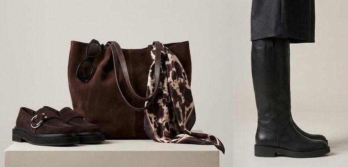 Botas negras de cuero hasta la rodilla combinadas con pantalones gris oscuro sobre un fondo beige liso.