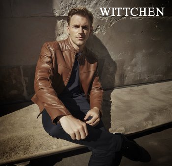 Brązowa skórzana kurtka o złożonej konstrukcji, z kołnierzem stójkowym i poziomymi przeszyciami. Model siedzący na teksturowej powierzchni.