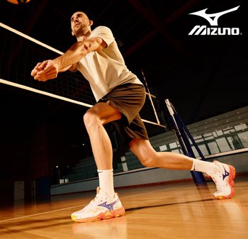 Zapatillas de voleibol Mizuno en blanco y naranja con acentos morados; un hombre con una camiseta clara y pantalones cortos se prepara para servir cerca de una red en una cancha.