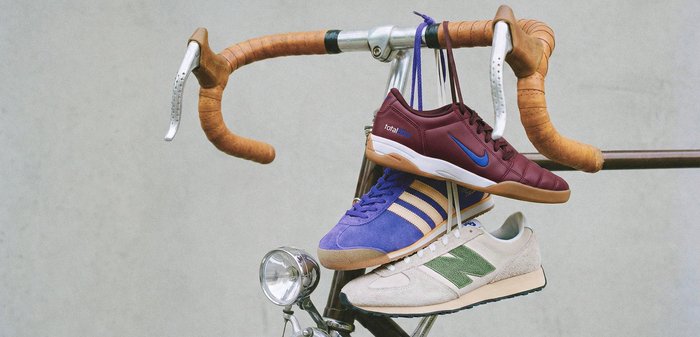 Trois paires de baskets — bordeaux, bleues et blanches avec du vert — suspendues par leurs lacets aux poignées en cuir d'un vélo vintage.