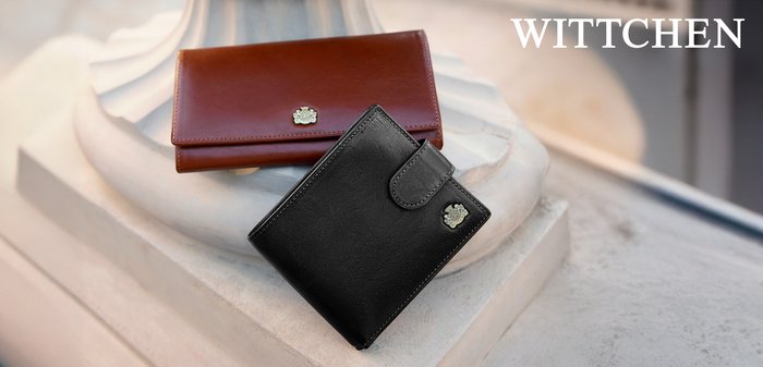 Dwa portfele wyeksponowane na kamiennej podstawce. Jeden jest z brązowej skóry i ma zapięcie, a drugi z czarnej skóry ma logo i strukturalne wykończenie.