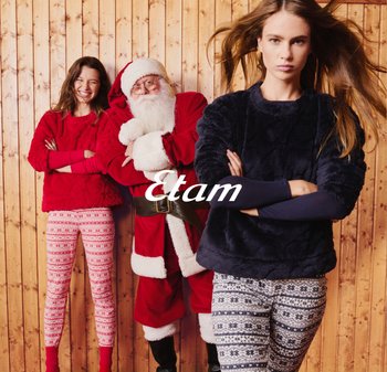 Dwie kobiety noszą przytulne swetry i wzorzyste legginsy, jedna w czerwonym, druga w granatowym. Mikołaj w czerwonym stroju stoi między nimi na tle drewnianej ściany.