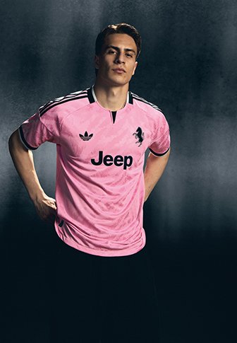 Junger Mann trägt ein pinkes Sporttrikot mit Jeep-Logo, steht mit den Händen in der Hüfte vor einem dunkelgrauen Hintergrund.