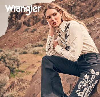 Wrangler-skjorta, ljusbeige med svarta kantdetaljer och knappar; mörkblå utsvängda jeans med vitt blommönster broderat på ena benet.