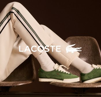 Zapatillas de ante verde con cordones blancos y suela blanca en contraste; pantalones crema con rayas laterales verdes y negras; sentado en una silla marrón.