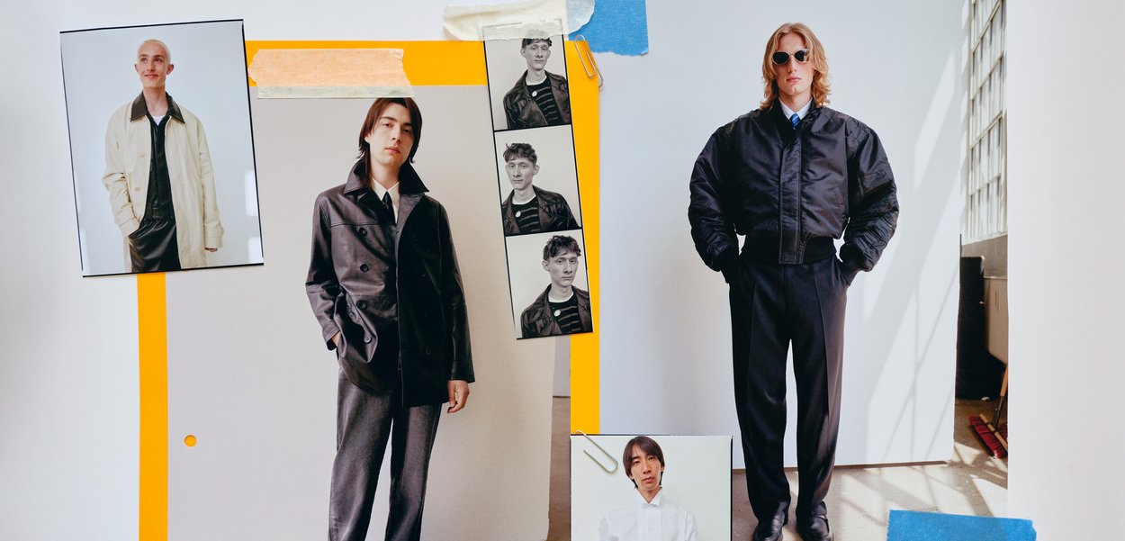 Two male models dressed in contemporary fashion: one in a black leather coat and the other in a cropped black bomber jacket and tailored trousers.