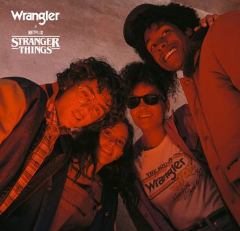 Fire unge mennesker smiler og lene seg i en sirkel, iført uformelle klær inspirert av 1980-tallet under rødt lys, med Wrangler- og Stranger Things-logoer.