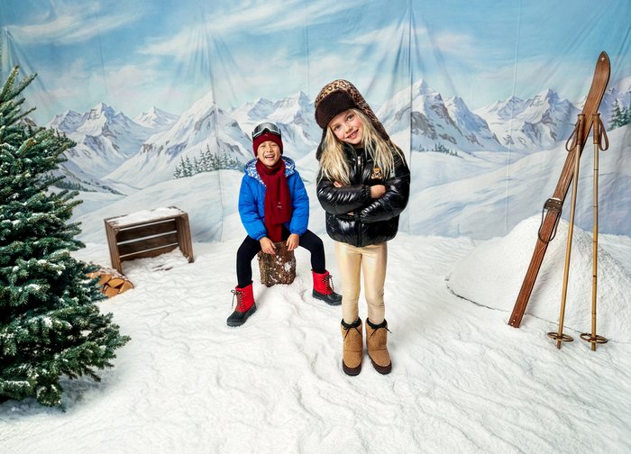 Deux enfants se tiennent sur un sol enneigé. L'un porte une veste bleue avec une écharpe rouge et des bottes rouges ; l'autre porte une doudoune noire et des bottes beige.