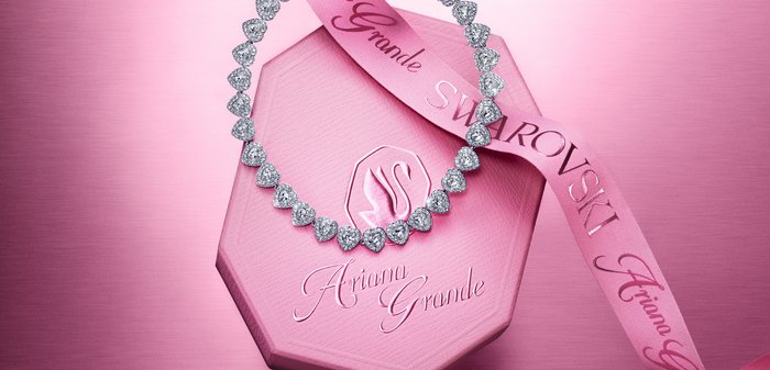 Hartvormige kristallen ketting op een roze achthoekige doos met een lint met de merken "Ariana Grande" en Swarovski.