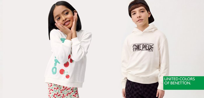 Dos niños, una niña con sudadera blanca con tomates y un niño con sudadera con capucha blanca con estampado de One Piece y gorra negra, están de pie contra un fondo blanco.